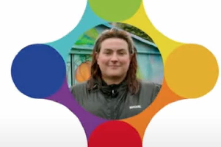 A women in a green coat smiles inside a colourful logo.