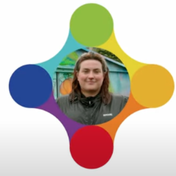 A women in a green coat smiles inside a colourful logo.